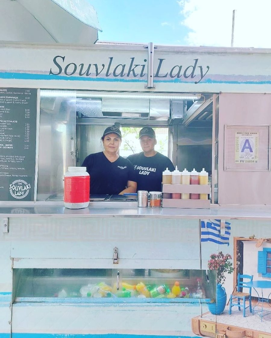 The Souvlaki Lady cart window with the team and a little blue Greek taverna corner on the sidewalk